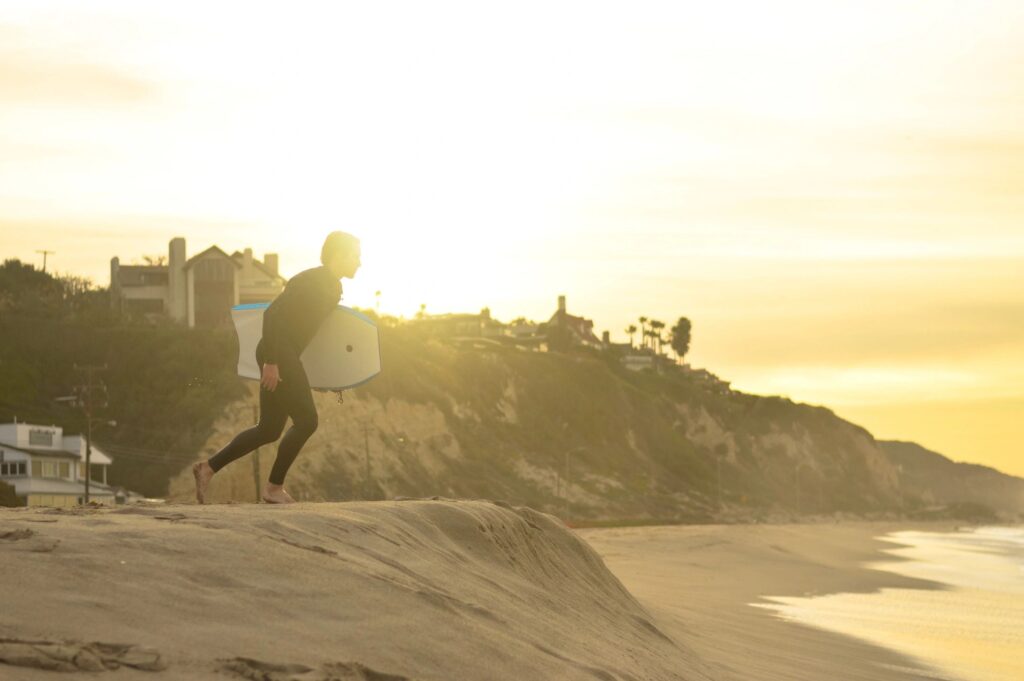 Motivation and yolo | Man with a surfboard walking on the beach toward the water. 