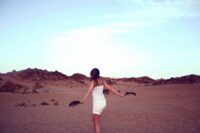 Beautiful lady in white dress, carrying black feathers walking toward a rocky hill.